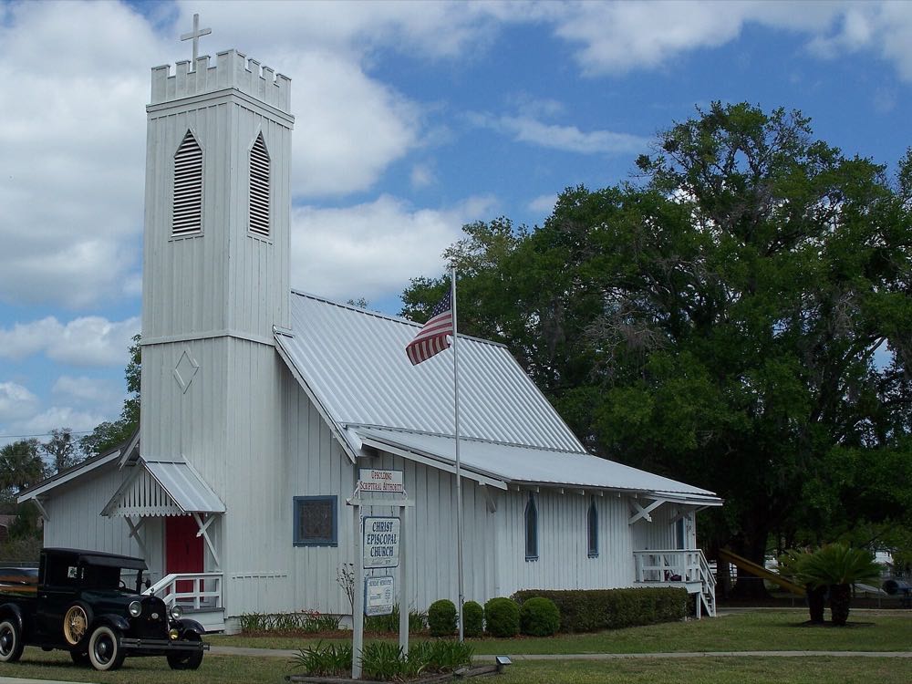 Christ Episcopal Church, a white board-and-batten church with a square bell tower, and a vintage pickup truck parked on the lawn