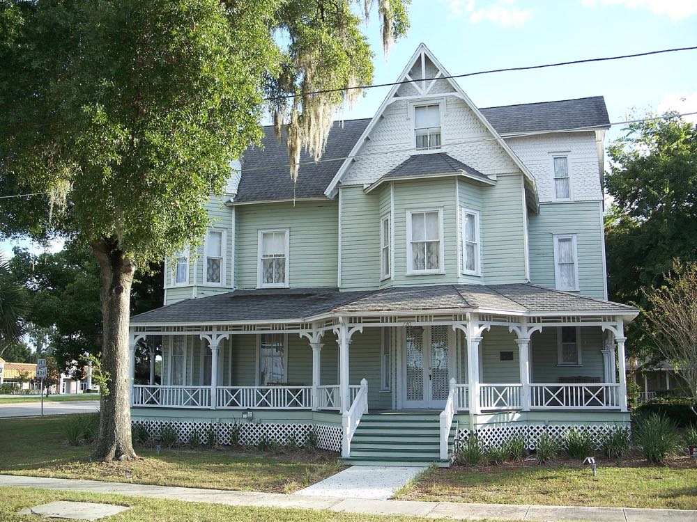 The Bradlee-McIntyre House, a pale green Victorian house with a wraparound porch, under a moss-hung oak