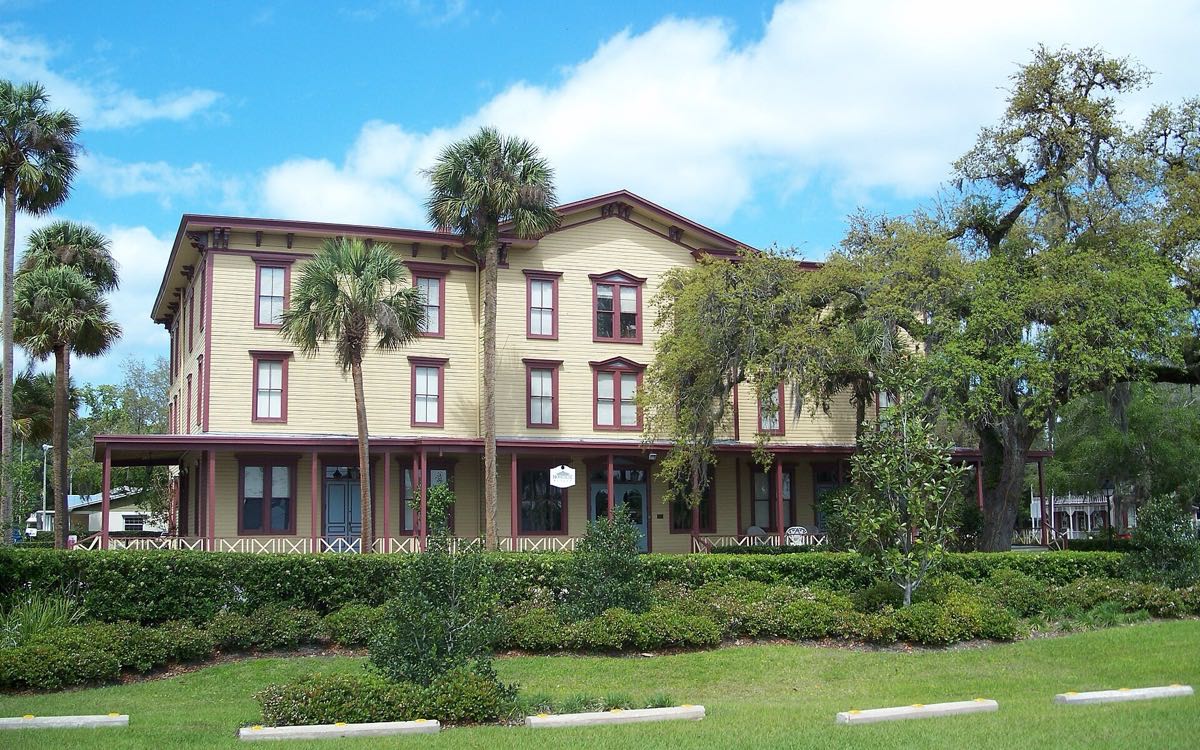 The Longwood Hotel, a three-story wooden building with a long front porch, behind palms and moss-hung oaks